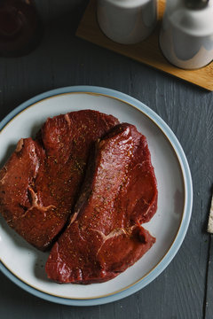 Two seasoned and oiled steaks ready for cooking.