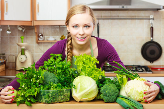 Smiling woman in kitchen with green vegetables