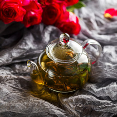 Glass teapot on a dark background. Red Roses nearby
