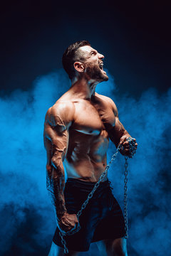 Side View Of Shirtless Muscular Man Screaming And Holding Chain.