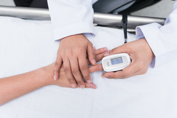 Doctor measuring blood oxygen levels of the sleeping elder patient on bed with oximeter.