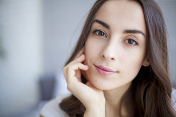 Portrait of Beautiful young brunette woman sitting at the end of the white bed.