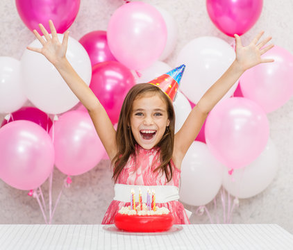 Happy girl in party hat with birthday cake lifted her arms in joy