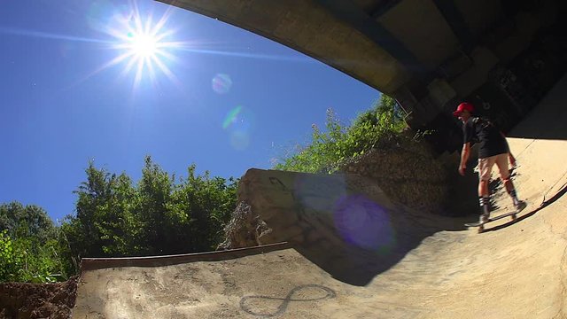 A Skateboarder rides a half pipe under an urban freeway underpass.