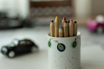 Colorful pencils in cup with kind of toys on background