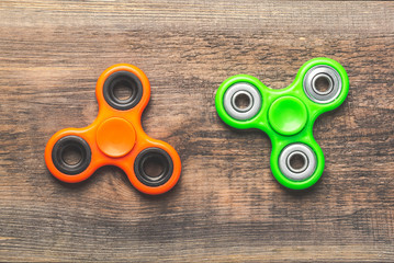 Orange and green fidget spinners close up on each other, stress relieving toys on wooden background.