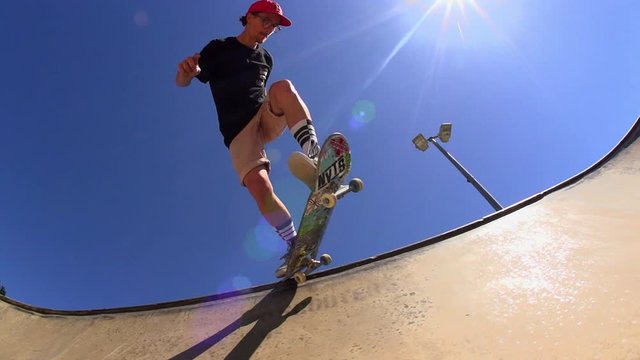A Skateboarder sliding along he lips of a bowl and then drops back in in slow motion.