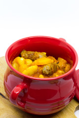 Butternut squash, pumpkin and bean stew with beef sausages. Red pot, white background. Isolated.
