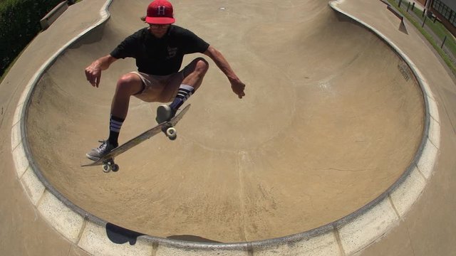 A Skateboarder riding a bowl jumps out in slow motion.