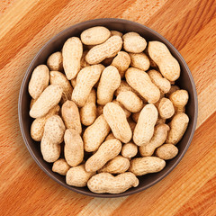 Delicious and healthy snack. Unshelled peanuts in ceramic bowl on wooden background closeup, top view