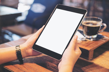 Mockup image of hands holding black tablet pc with blank white screen with coffee and tea on wooden table in cafe