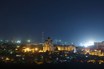 The bright lights of the city streets in the background of the night sky. The Orthodox Church in a residential area.