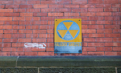 Old faded Fallout Shelter Sign on grungy red Brick Wall background