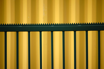 Spitzgezackter Zaun vor Container / Die Seitenansicht gelben Cargo Containers vor dem sich ein markanter spitzgezackter grüner Zaun befindet.