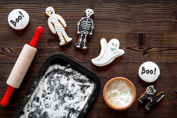 Cook halloween gingerbread cookies in shape of skeleton, ghost. Sweets near desk and rolling pin. wooden background top view copyspace