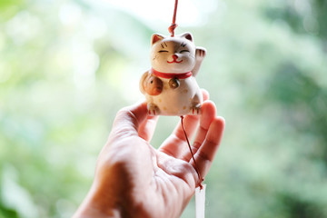 Woman hand is holding a Japan lucky cat doll is hanging on the window