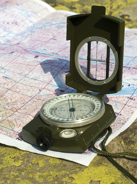a compass and a mountain map lying on a lichen-covered natural boulder