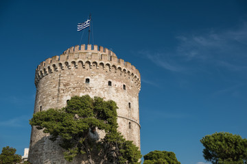 Fototapeta na wymiar Ancient stone tower with Greek flag on the top