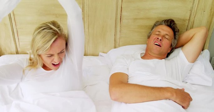 Woman getting irritated while man snoring on bed 