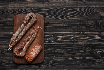 Three types of dried sausage on cutting board.Top view/Three types of chorizo on a rustic chopping board on dark wooden table