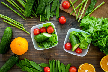 Healthy meal in containers. Salad with tomato, cucumber, orange in containers on wooden background top view