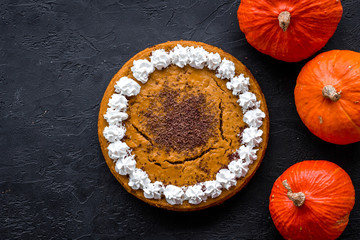 Fototapeta premium Homemade pumpkin pie decorated whipped cream and chocolate near pumpkins on black background top view copyspace