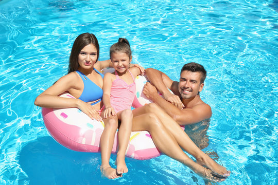 Young couple and cute daughter with inflatable ring in swimming pool