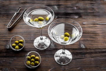 Make martini cocktails. Glass with beverage, olives and utensils on dark wooden background top view