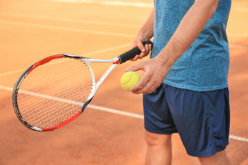 Man with tennis racket and ball standing on court
