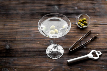 Make martini cocktails. Glass with beverage, olives and utensils on dark wooden background top view copyspace