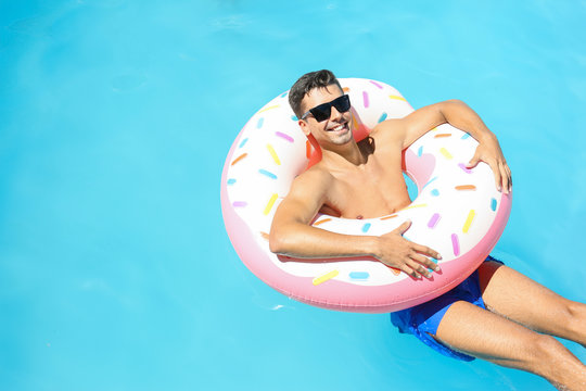 Young man with inflatable donut in swimming pool