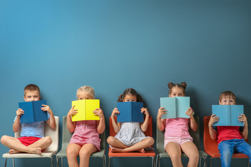 Cute little children reading books while sitting near color wall - obrazy, fototapety, plakaty