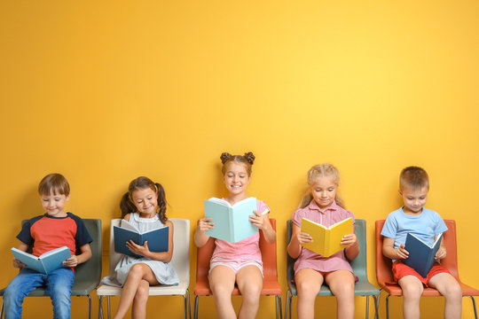 Cute little children reading books while sitting near color wall