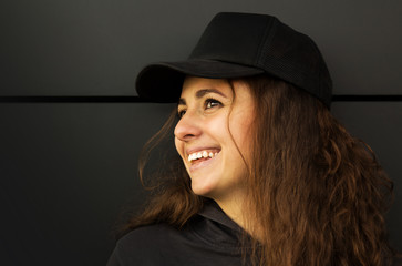 Portrait of a trendy happy teenager girl or woman in a cap stands on a grey background