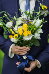 Closeup of beautiful bouquet of fresh colorful flowers in male hands. Man wearing blue formal suit...