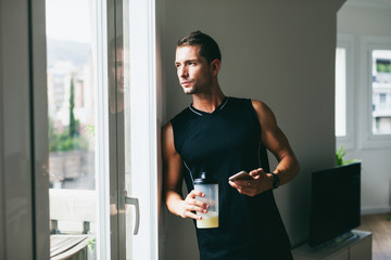 Young man using his phone whilst drinking a protein shake after hard workout.