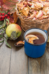  Compote of apples in a blue enamel mug and slices of dry apples in a wicker brown basket on an old wooden table. The concept of healthy eating.
