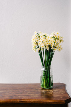 jonquils in a vase on a timber table agains a plain wall