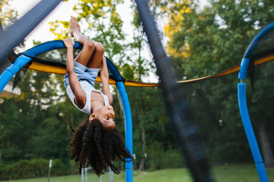 A young girl hanging upside down on a trampoline