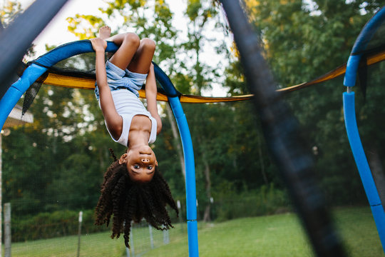 A young girl hanging upside down on a trampoline