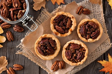 Mini pecan pie tarts, above view table scene on a rustic wood background