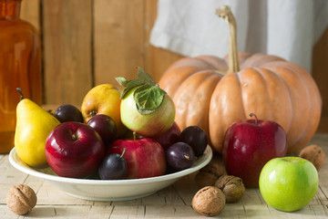 Autumn still life with apples, pears, plums, pumpkin and walnuts on a wooden background. Rustic style, selective focus.