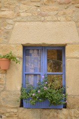 Fototapeta na wymiar Flowers pot on blue window in Peratallada, Girona, Spain