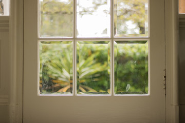 A front glass door to a house is closed. View from inside. We can see a blurred green nature from an outside.