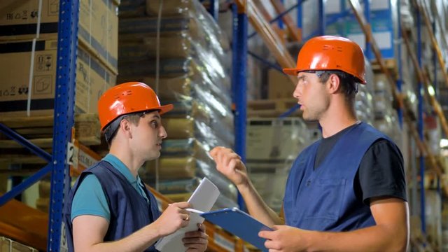 Two warehouse workers point and discuss storage items.