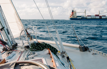 Bow of sailboat on ocean voyage passing shipping container