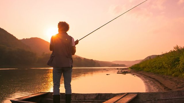 Stylish guy fishing from a boat to a pond at sunset