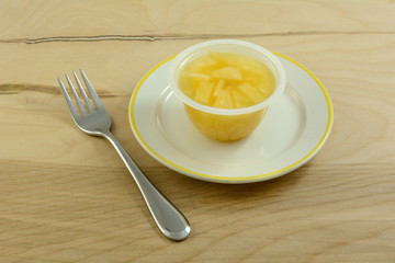 Chopped pineapple in juice in plastic snack container on plate with fork
