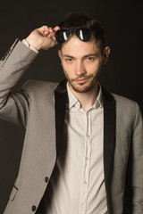 portrait of a young man with an unshaven face in a suit wearing black glasses with a pensive face on a dark background