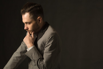 Fototapeta premium young serious man with an unshaven face in a suit with a pensive face on a dark background